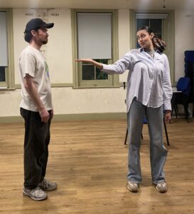 Female actor gestures towards a male actor, both standing