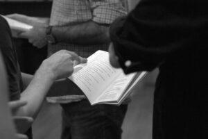 Image of a hand pointing to a point in a script, with actors standing nearby